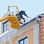 Workers clean snow and  icicle  from a house roof